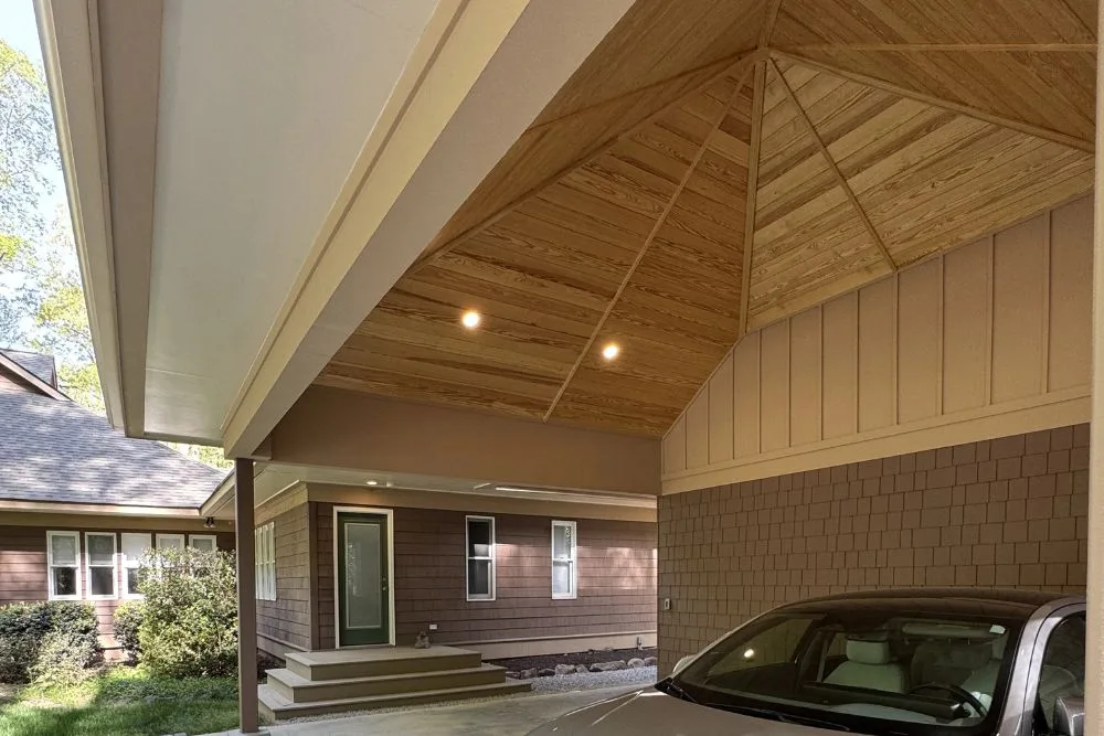 Attached carport with vaulted shiplap wood ceiling and a parked silver car under it.