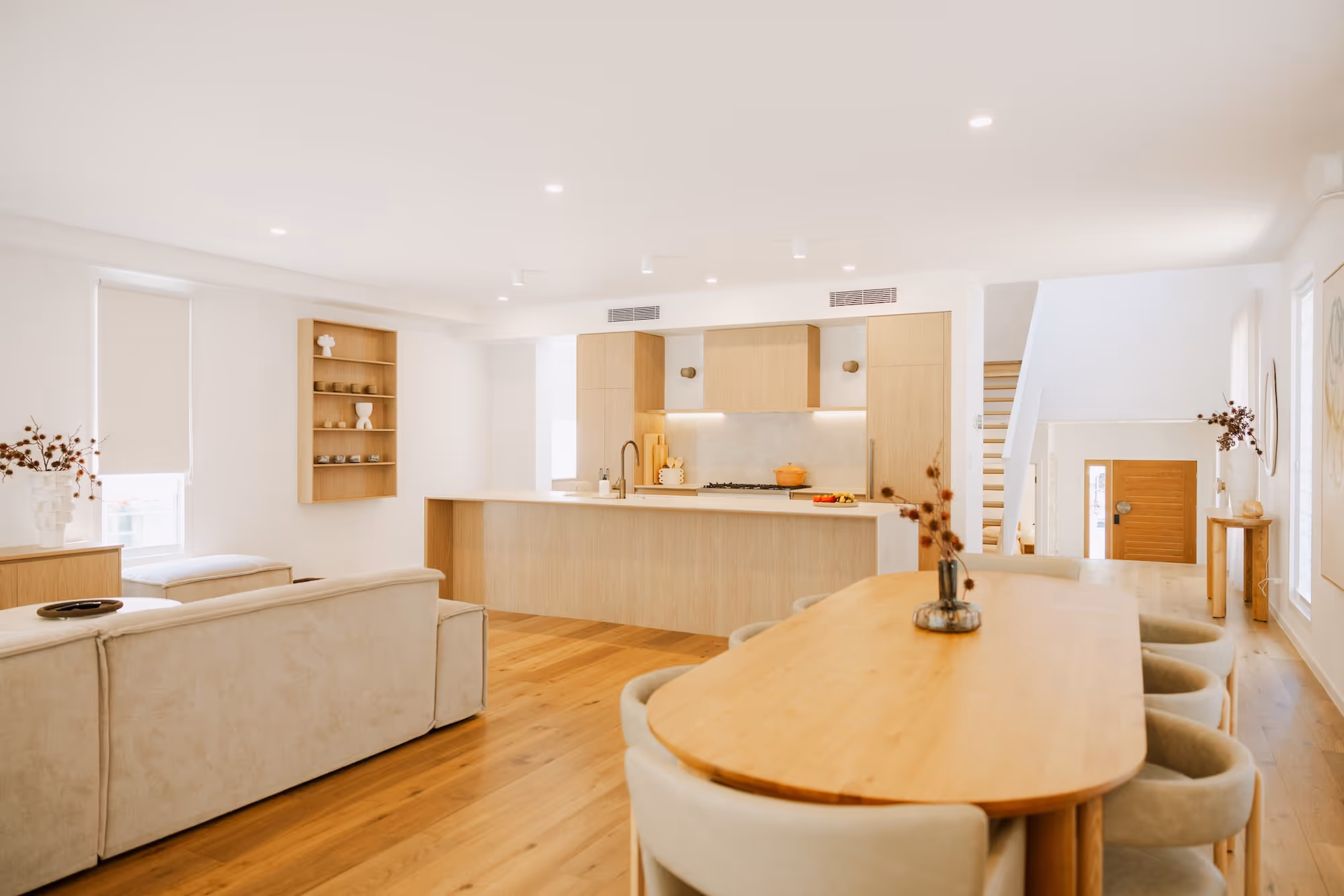 Modern open-plan kitchen and dining area with light wood furniture and beige seating.
