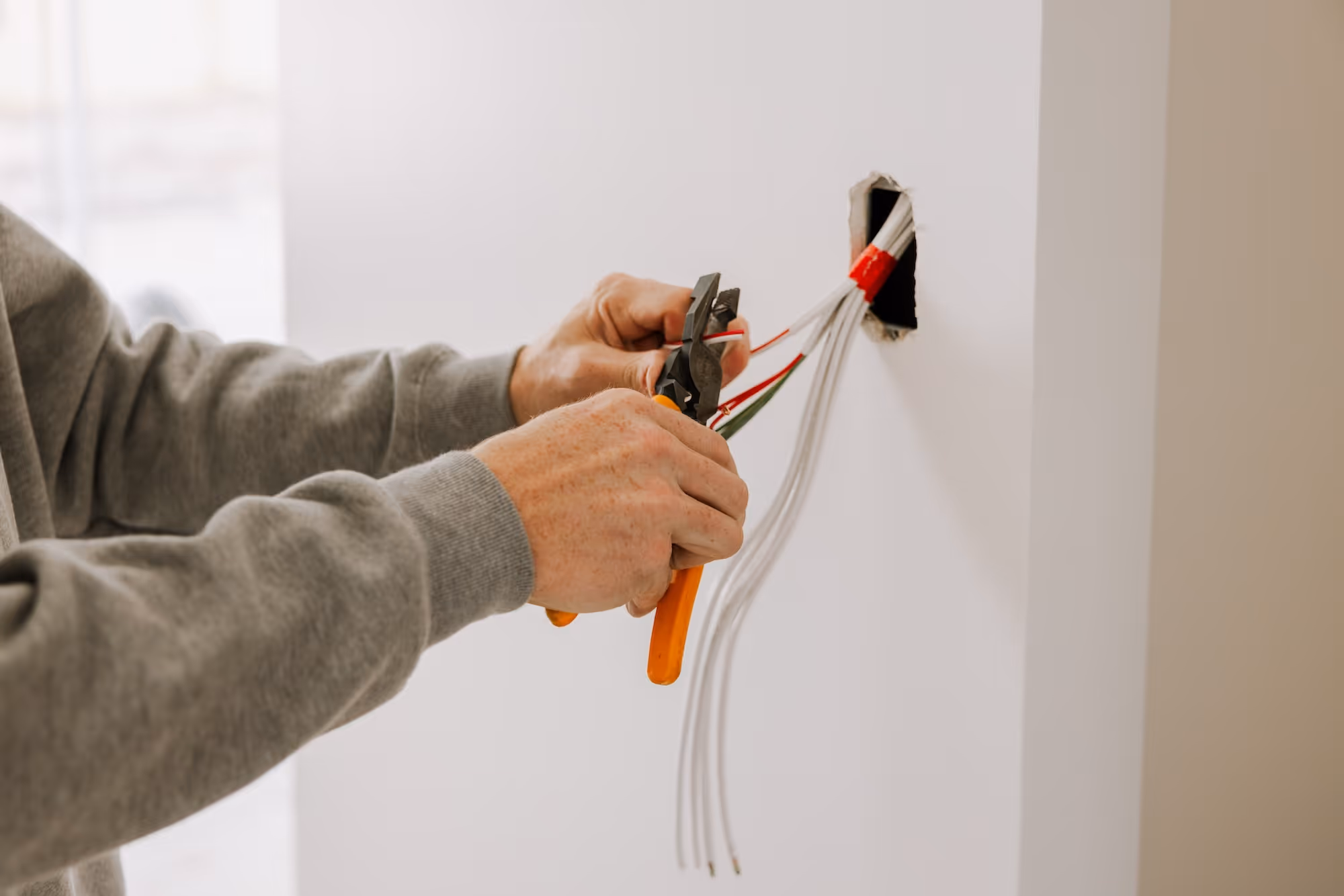 Close-up of a person using wire cutters to handle electrical wires inside a wall outlet.
