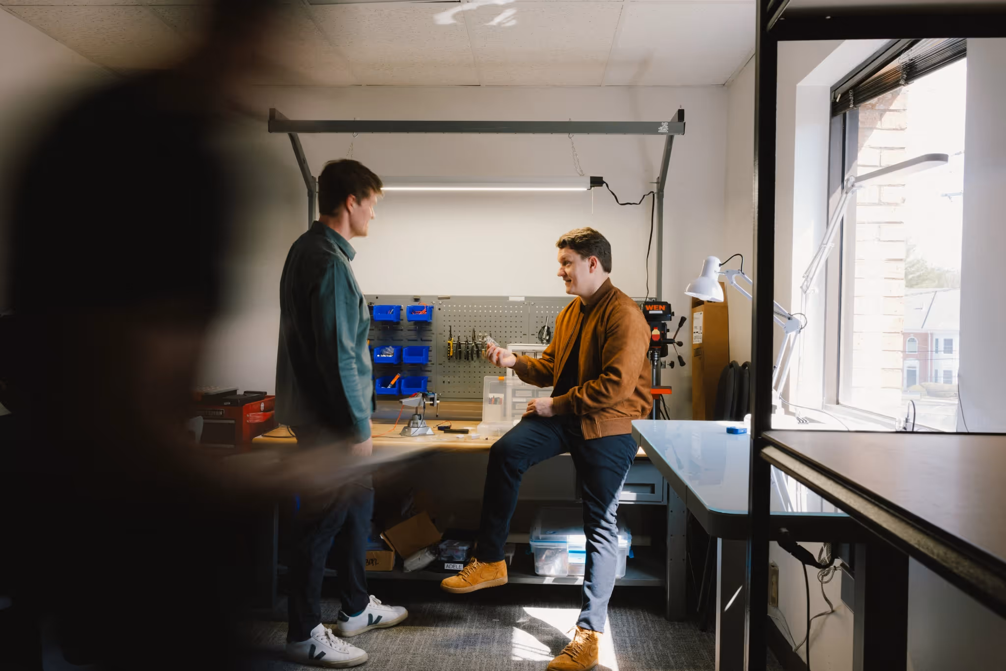 Two male coworkers at Adele Health discussing a design at a workbench in their office.