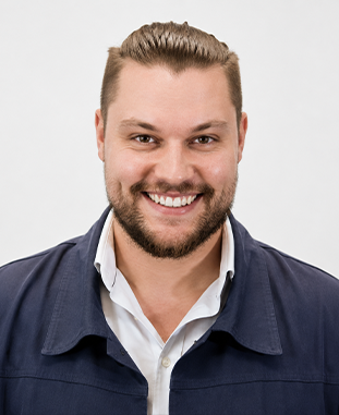 Uśmiechnięty mężczyzna z krótkimi brązowymi włosami i brodą w czarnej koszulce.