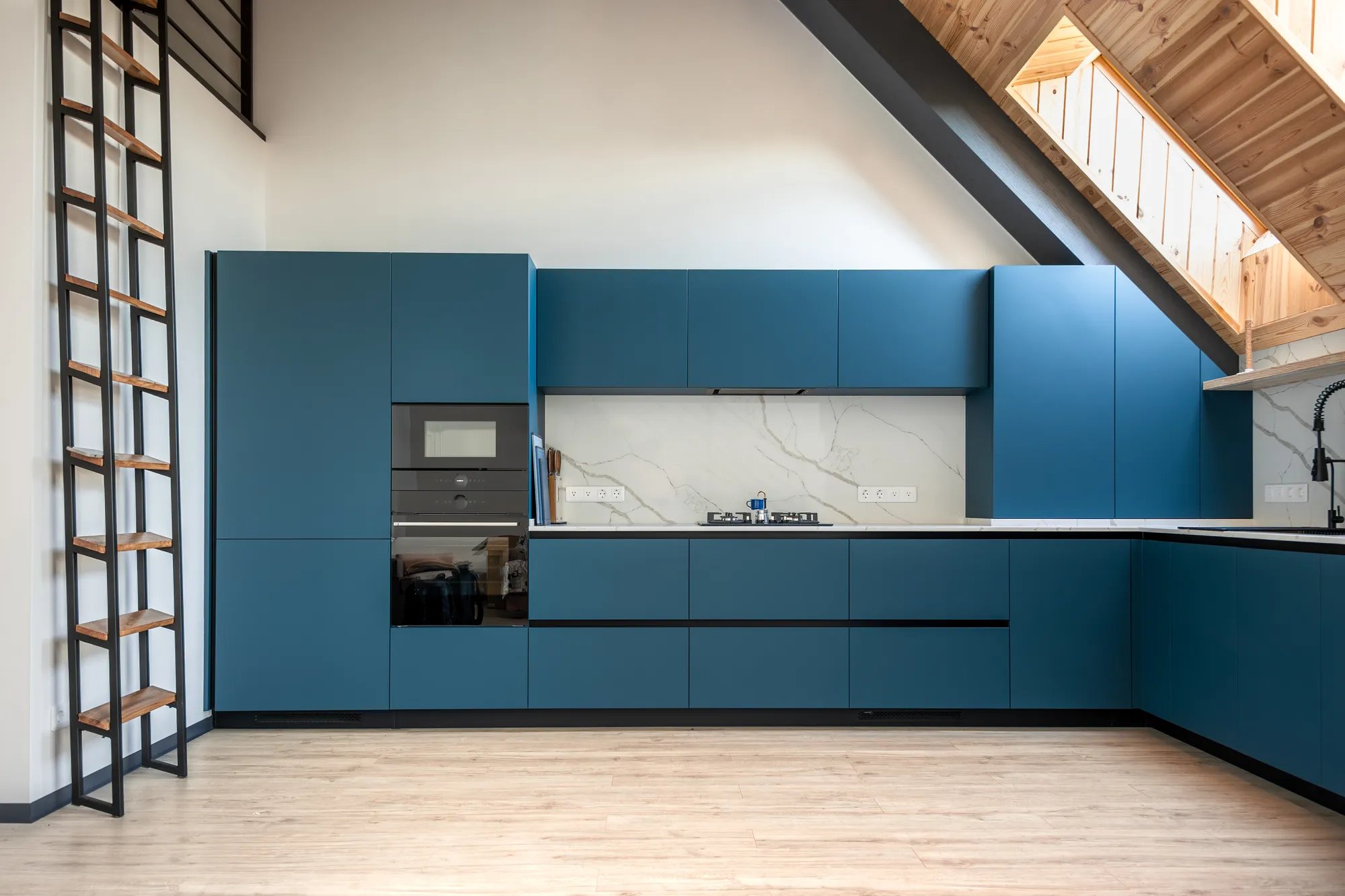 Modern kitchen with blue cabinets in a room with a sloped wood-beam ceiling and a ladder
