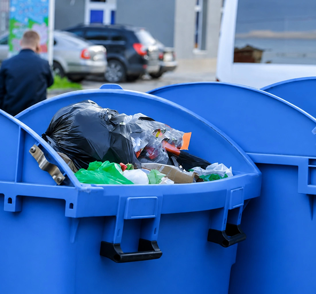 Blue recycling bin filled with mixed plastic bags and waste