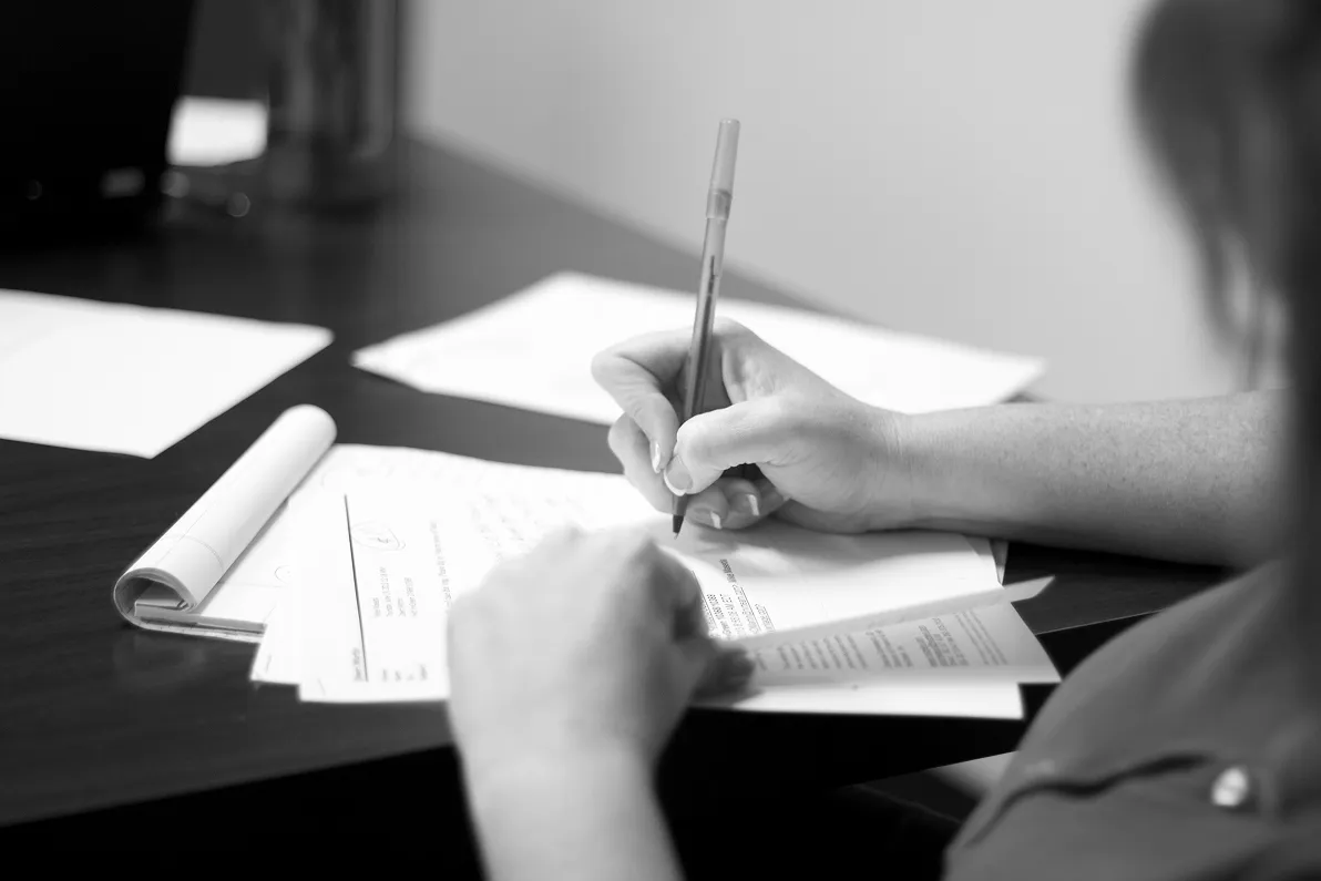Black and white closeup of a person's hands writing or reviewing documents