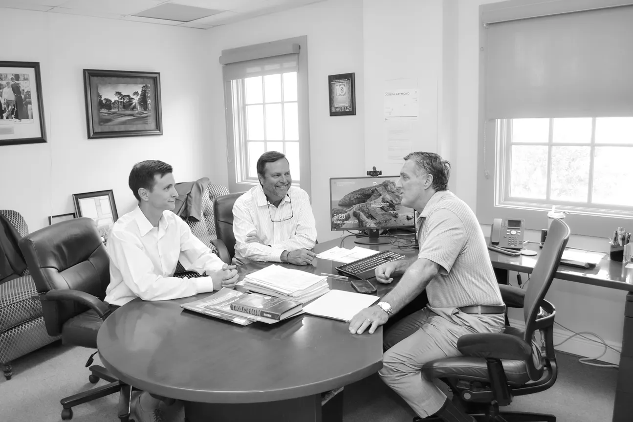 Black and white photo of three men in a business meeting around a round office table