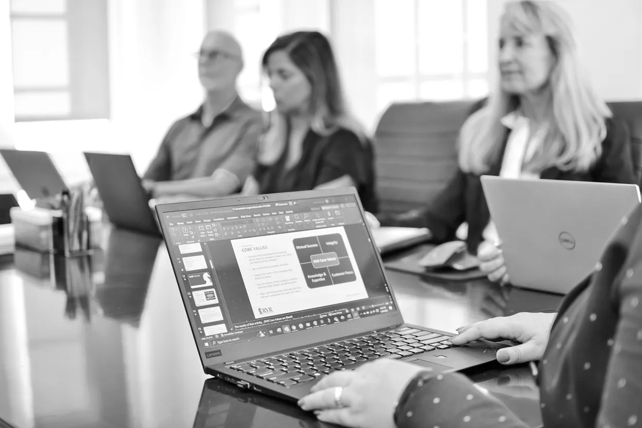 Black and white photo of professionals at a meeting table with a laptop displaying a website