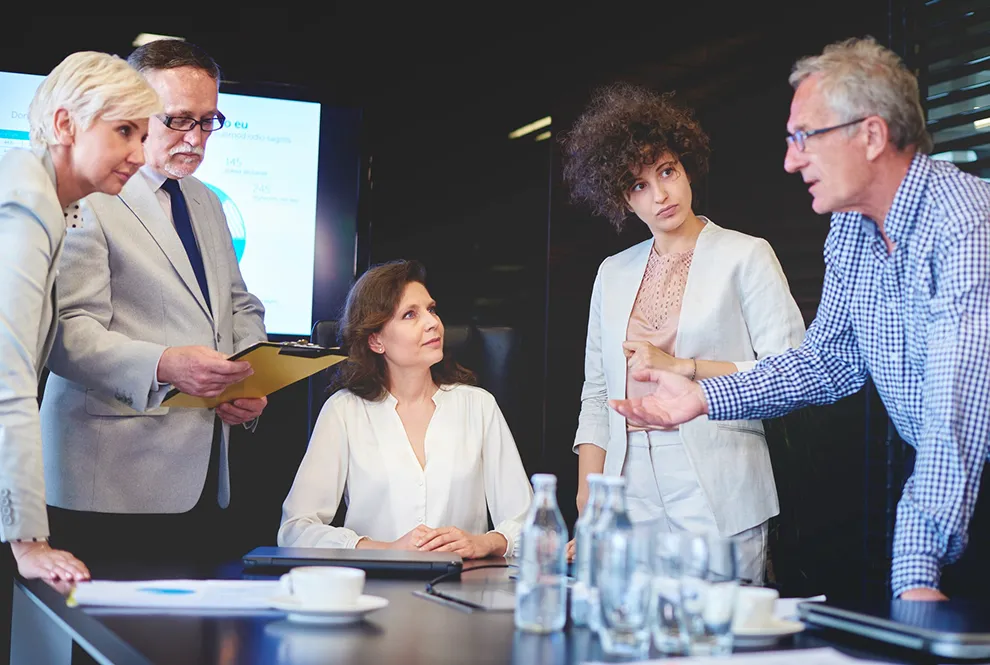 A group of professionals in a business meeting, with a man presenting to colleagues at a conference table