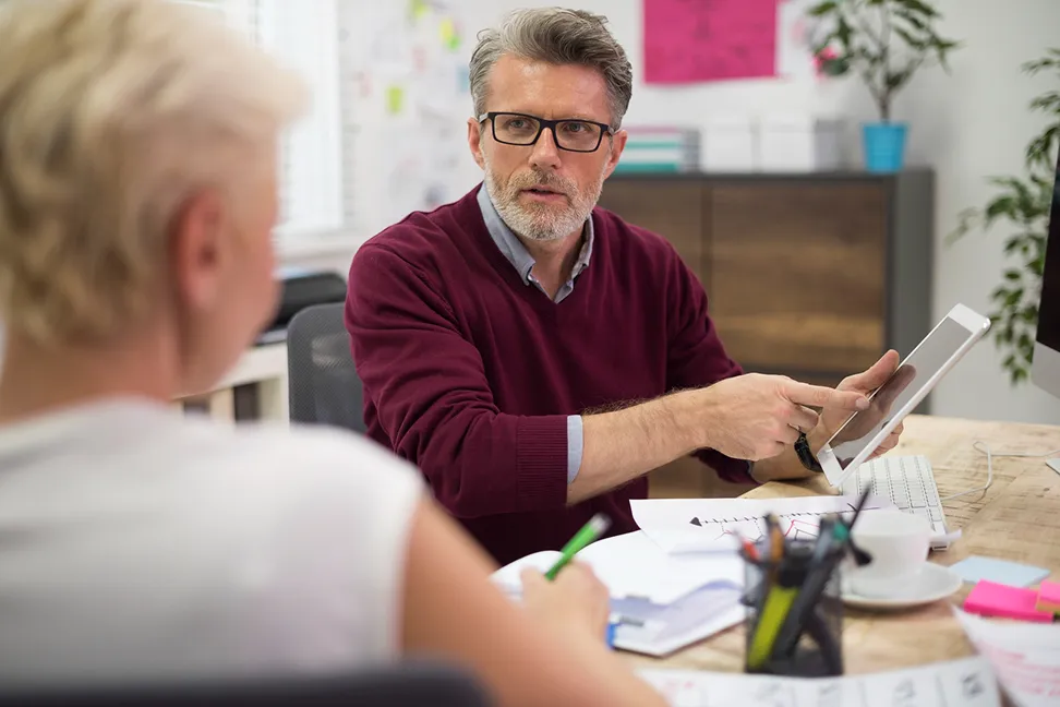 A man in a dark red sweater sitting at a desk during a professional meeting or consultation