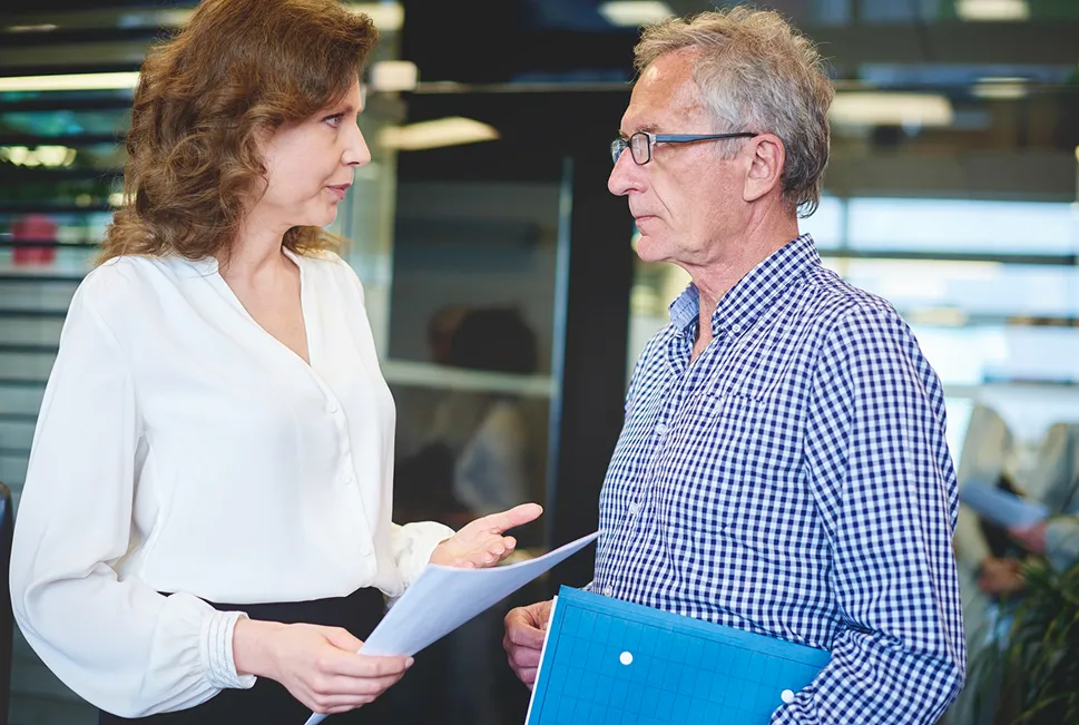 A woman and an older man in glasses having a professional discussion, reviewing documents