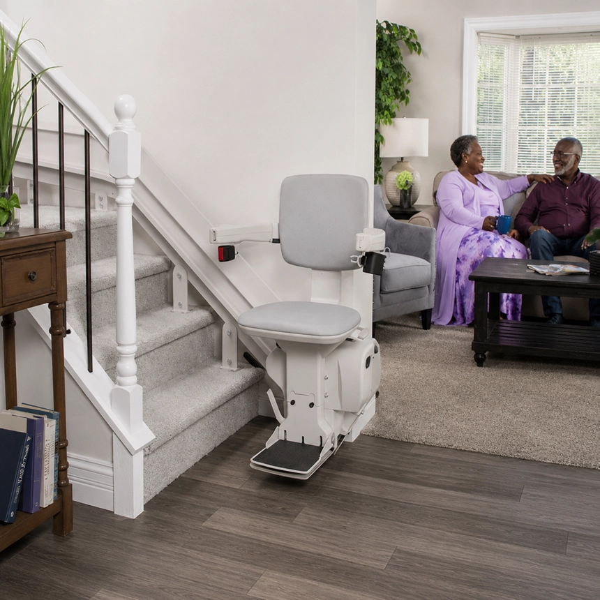 Bruno Elite curved stair lift installed on a carpeted staircase in a home with a senior couple sitting in the background.