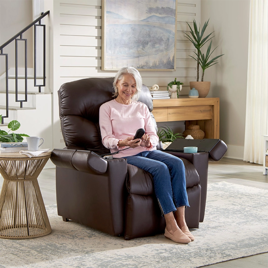 An older woman smiling while using a remote control in a brown leather power lift recliner by Simple Comforts.