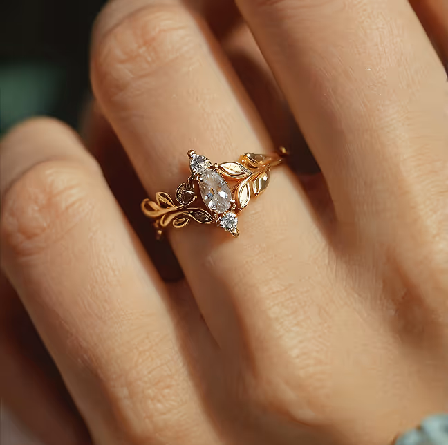 Close-up of a hand wearing a gold ring with a marquise diamond and leaf-shaped details.