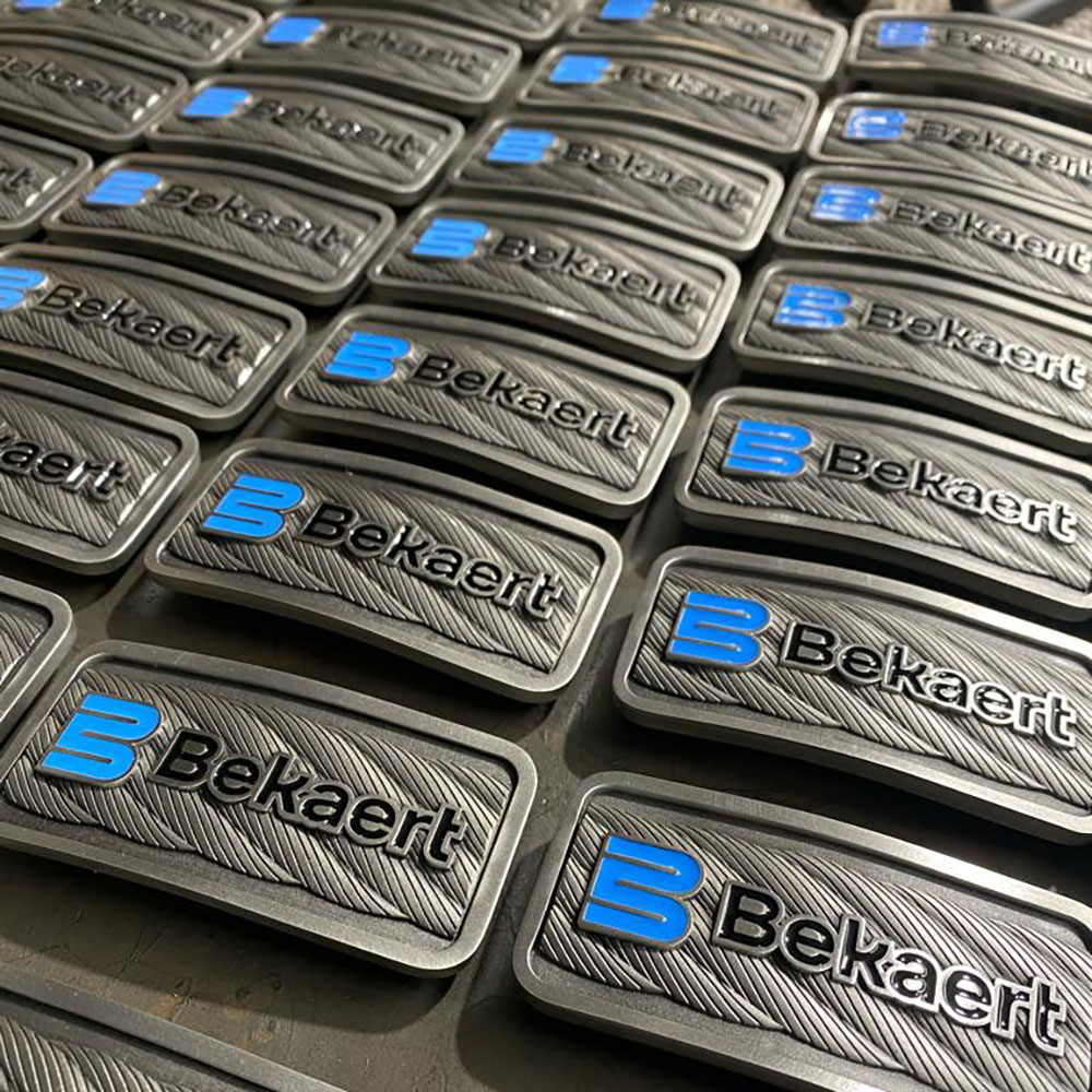 Batch of custom branded pewter belt buckles arranged in production rows, representing larger workforce and organisational recognition programs.