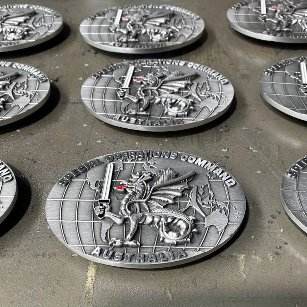 Grouped custom pewter challenge coins and buckles during production, representing mid-scale operational and organisational recognition orders.