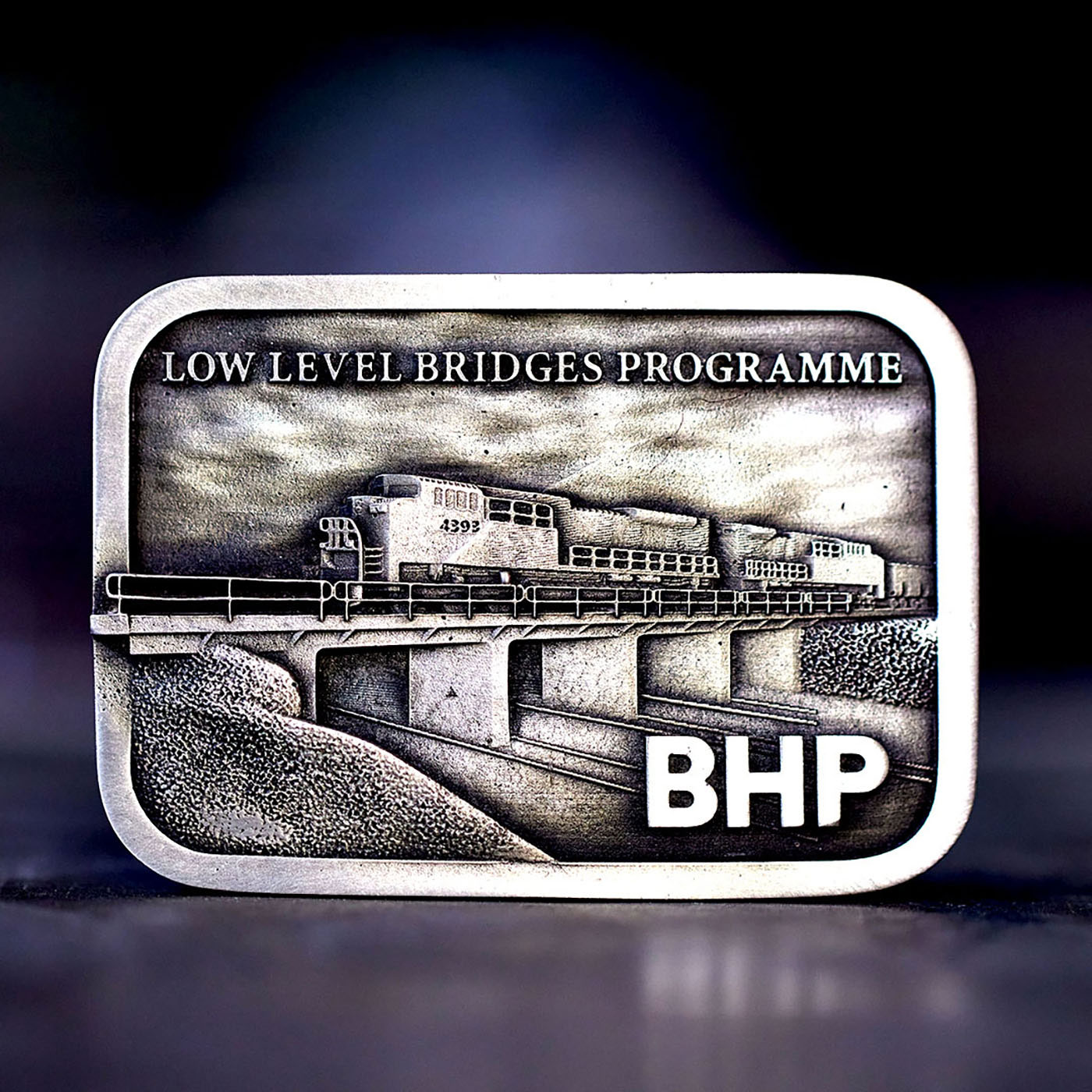 Custom BHP Low Level Bridges Programme belt buckle featuring rail infrastructure artwork