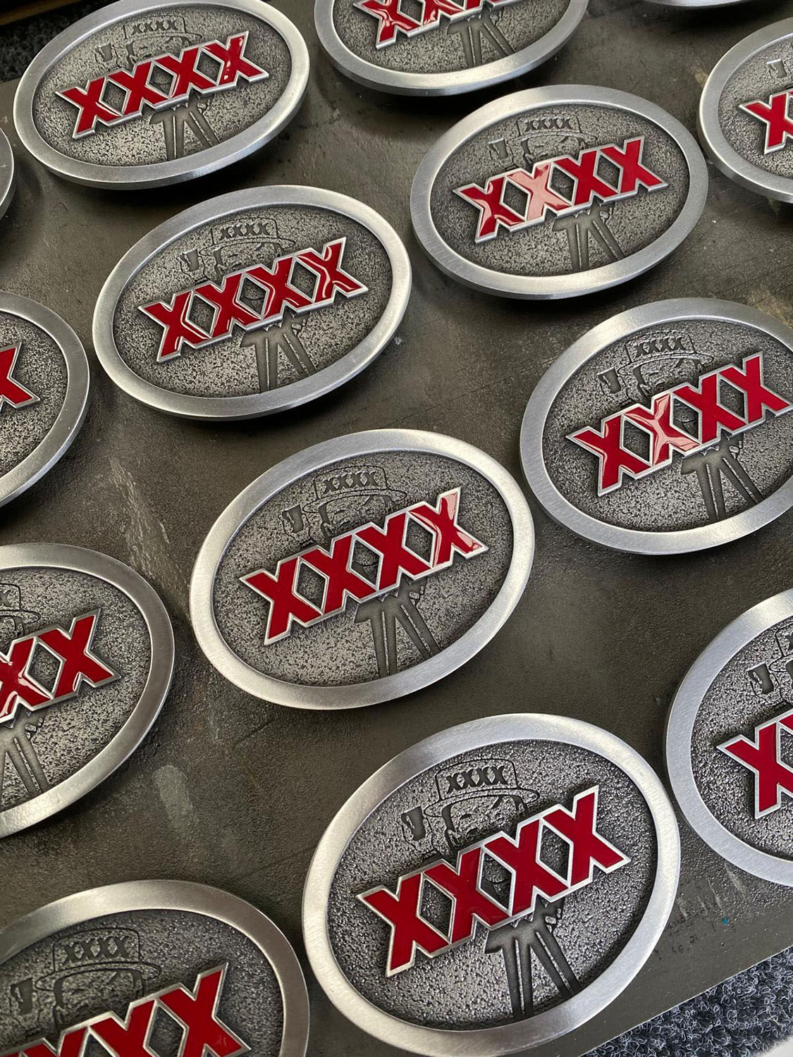 XXXX promotional belt buckles produced in custom pewter with red enamel accents