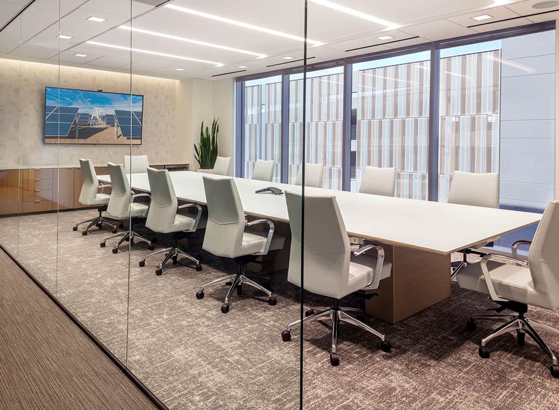 Modern conference room with white chairs around a long table and large windows with city views.