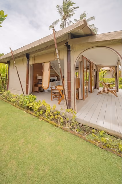 Open-air luxury tent with wooden furniture and green lawn in tropical setting.