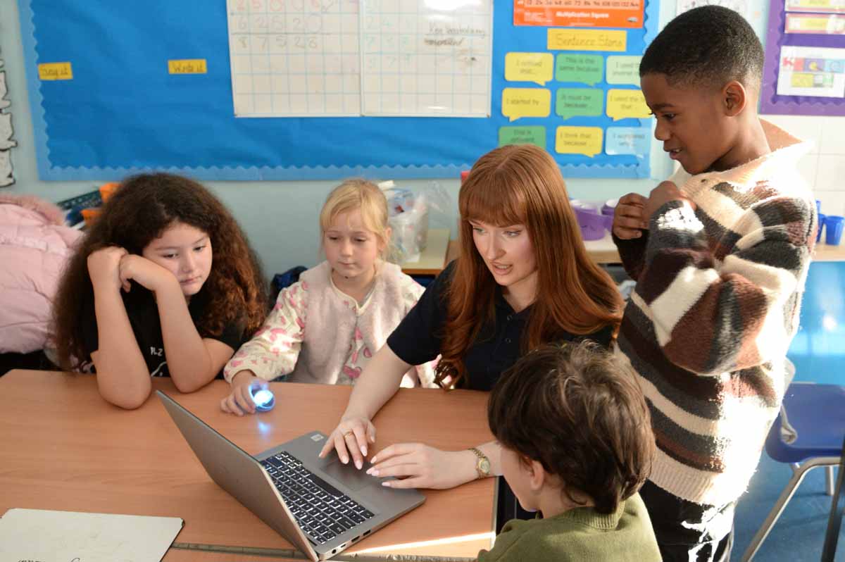 Two children seated at desks using computers with a retro-style platform video game displayed on both monitors.