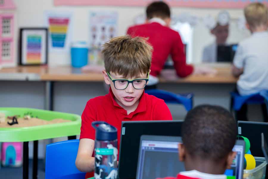 Two children seated at desks using computers with a retro-style platform video game displayed on both monitors.