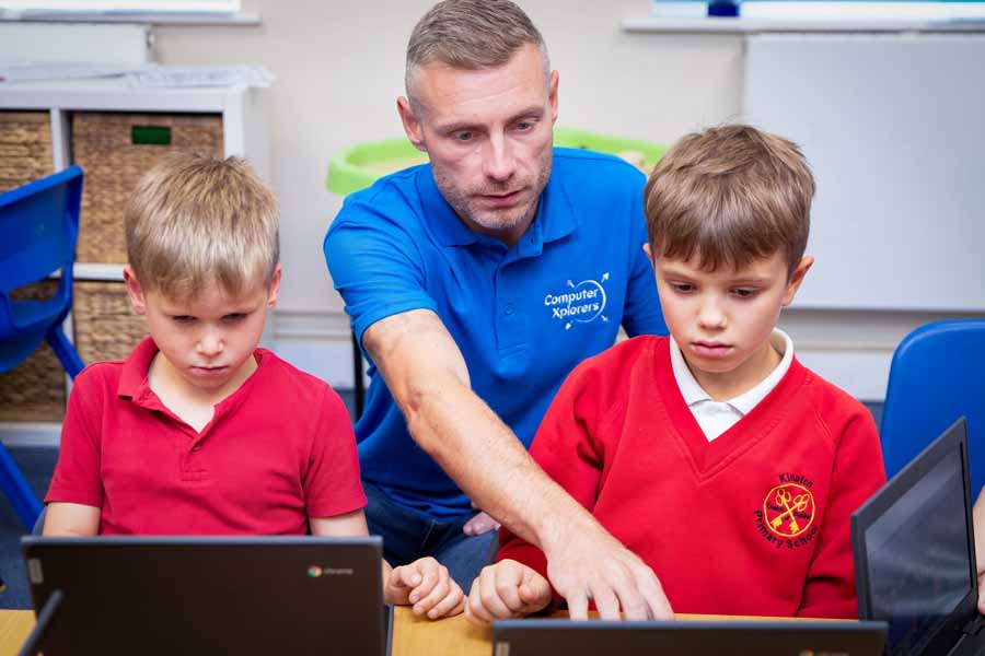 Child using a laptop with a visual programming interface on screen, sitting at a desk with a red Angry Birds water bottle.