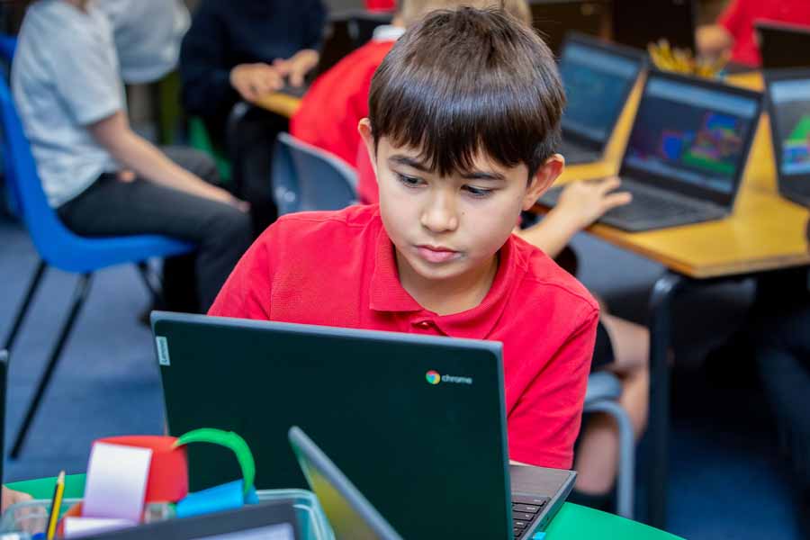 Child using a laptop with a visual programming interface on screen, sitting at a desk with a red Angry Birds water bottle.