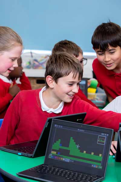 Two children seated at desks using computers with a retro-style platform video game displayed on both monitors.