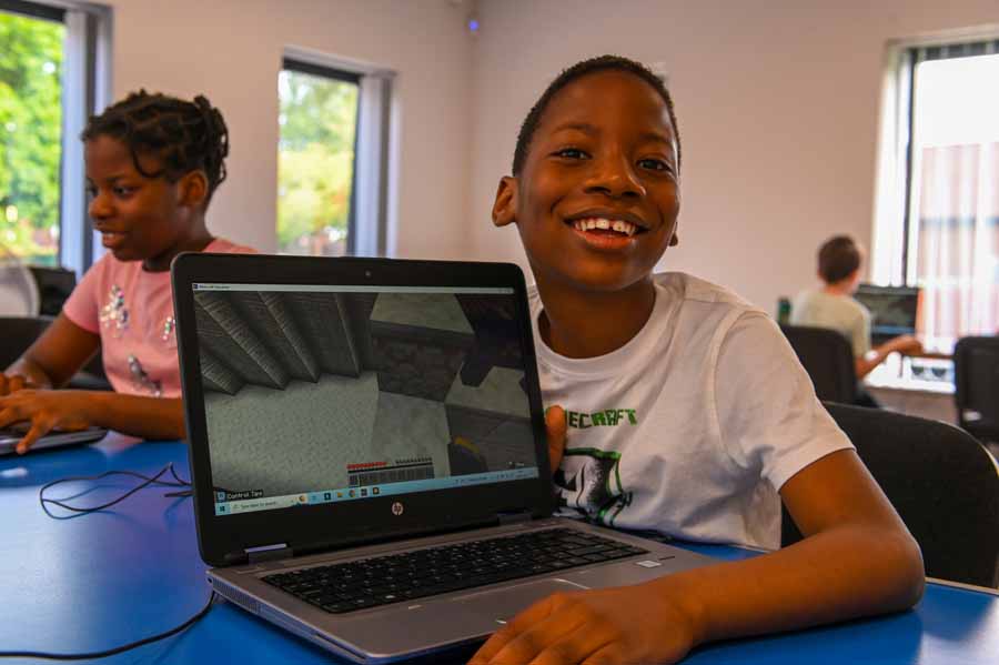 Two children seated at desks using computers with a retro-style platform video game displayed on both monitors.