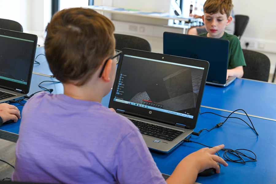 Two children seated at desks using computers with a retro-style platform video game displayed on both monitors.