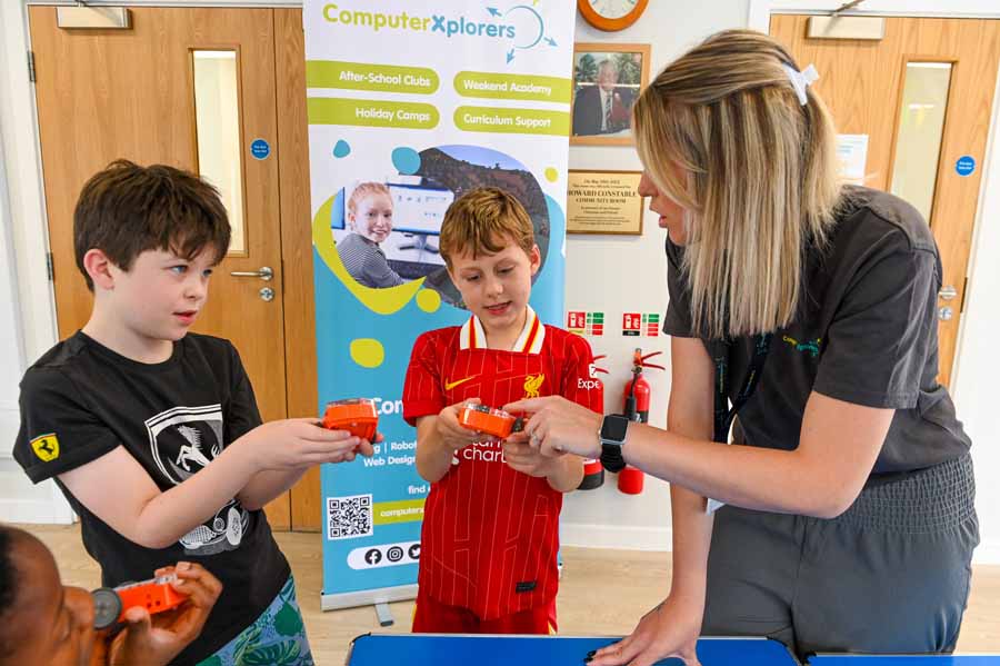 Adult male in a blue Computer Xplorers shirt helping a young boy in a red sweater with a laptop.