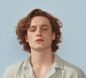 Young man with wavy brown hair and light shirt against a pale blue background.