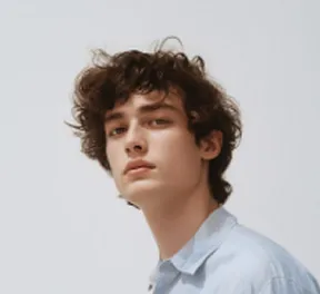 Young man with curly dark hair wearing a light blue shirt against a plain background.