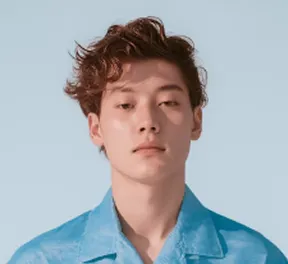 Young man with curly hair wearing a blue shirt against a light blue background.