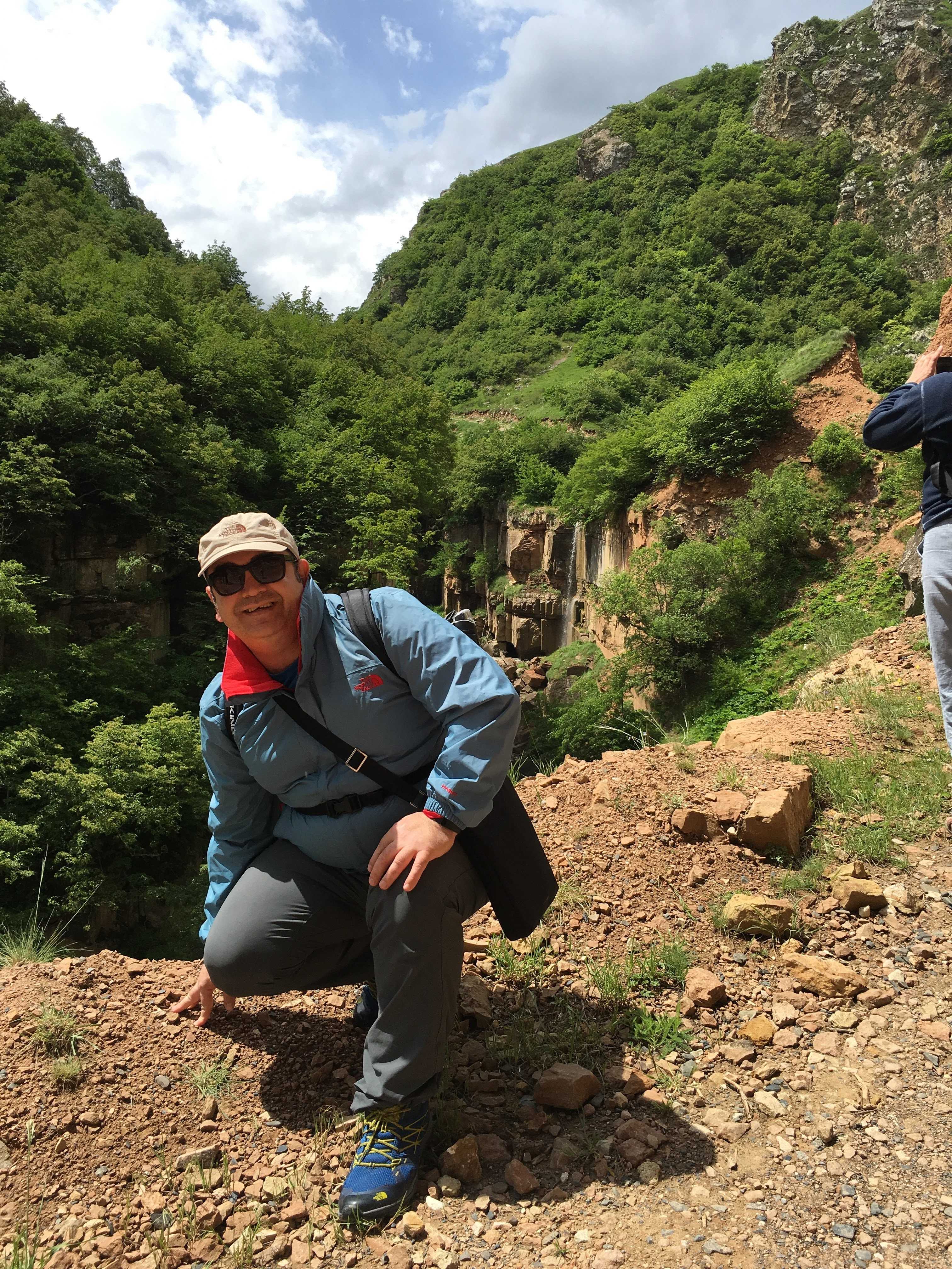 The founder in a green mountain gorge in the Caucasus, waterfall beyond — from the founder's archive.