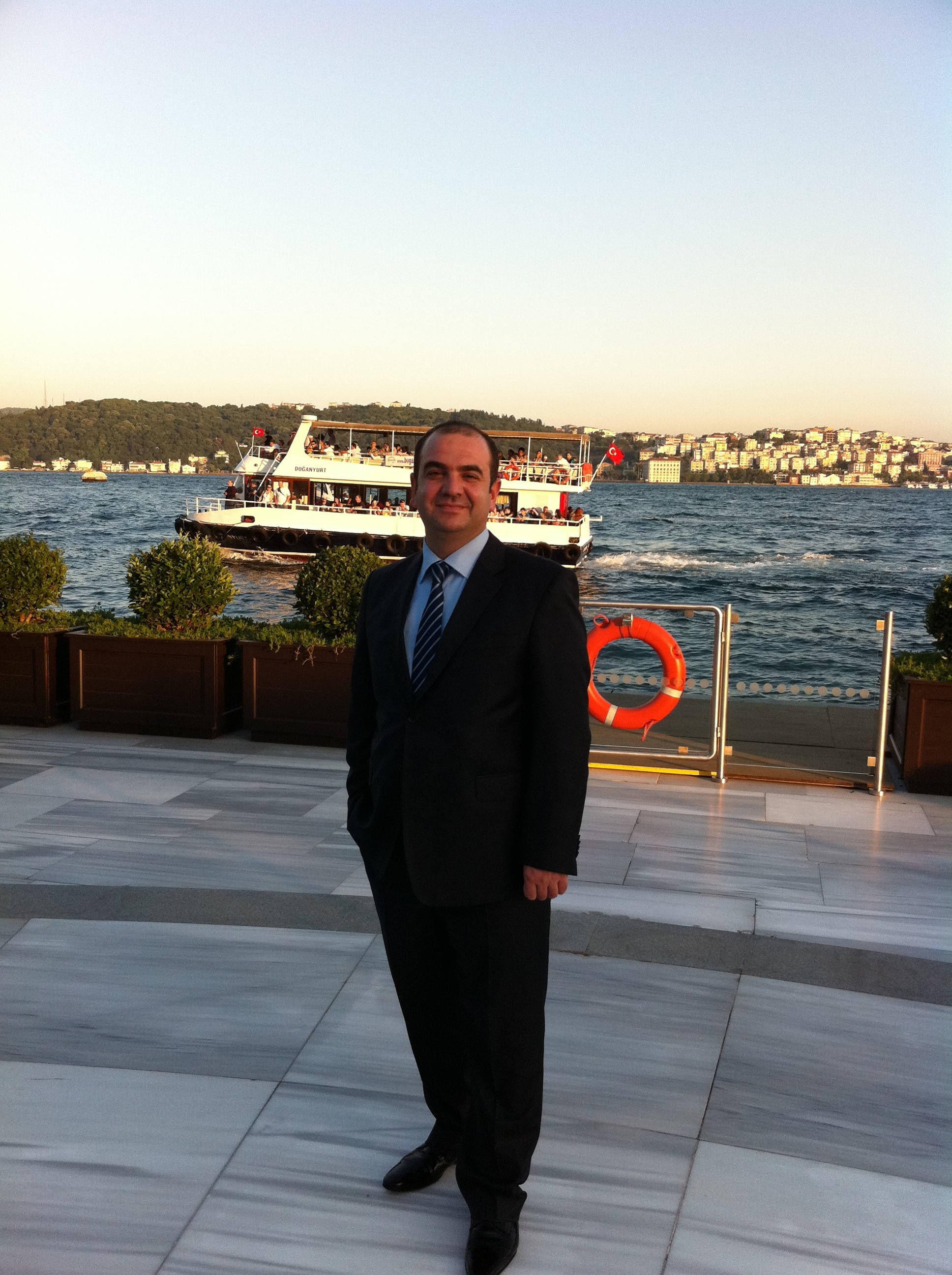 The founder on a Bosphorus-side terrace at dusk, the Doğanyurt ferry passing behind him, Istanbul.