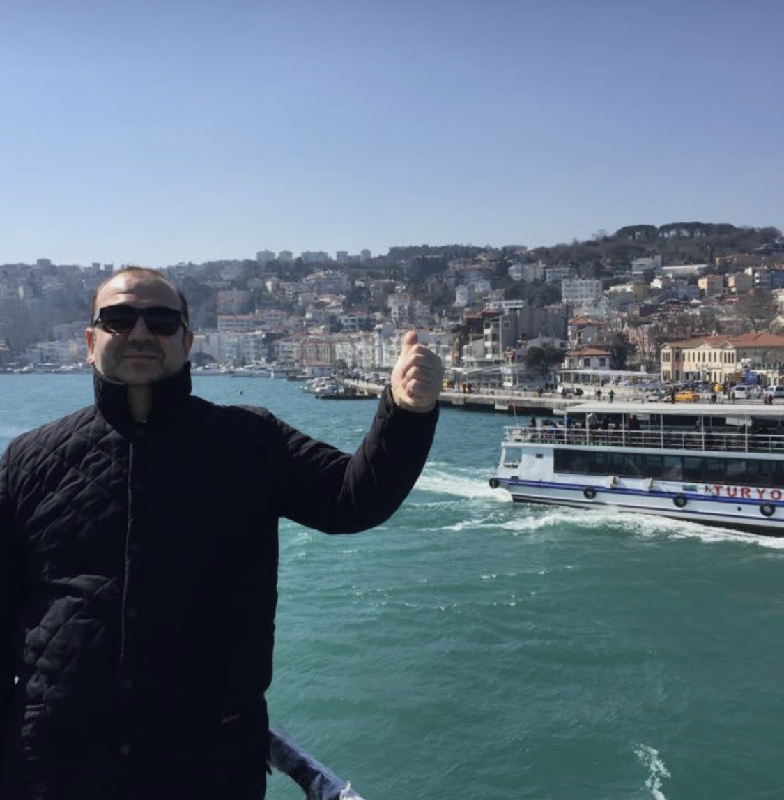 The founder giving a thumbs up on a Bosphorus ferry, Istanbul's hillside neighborhoods behind him.