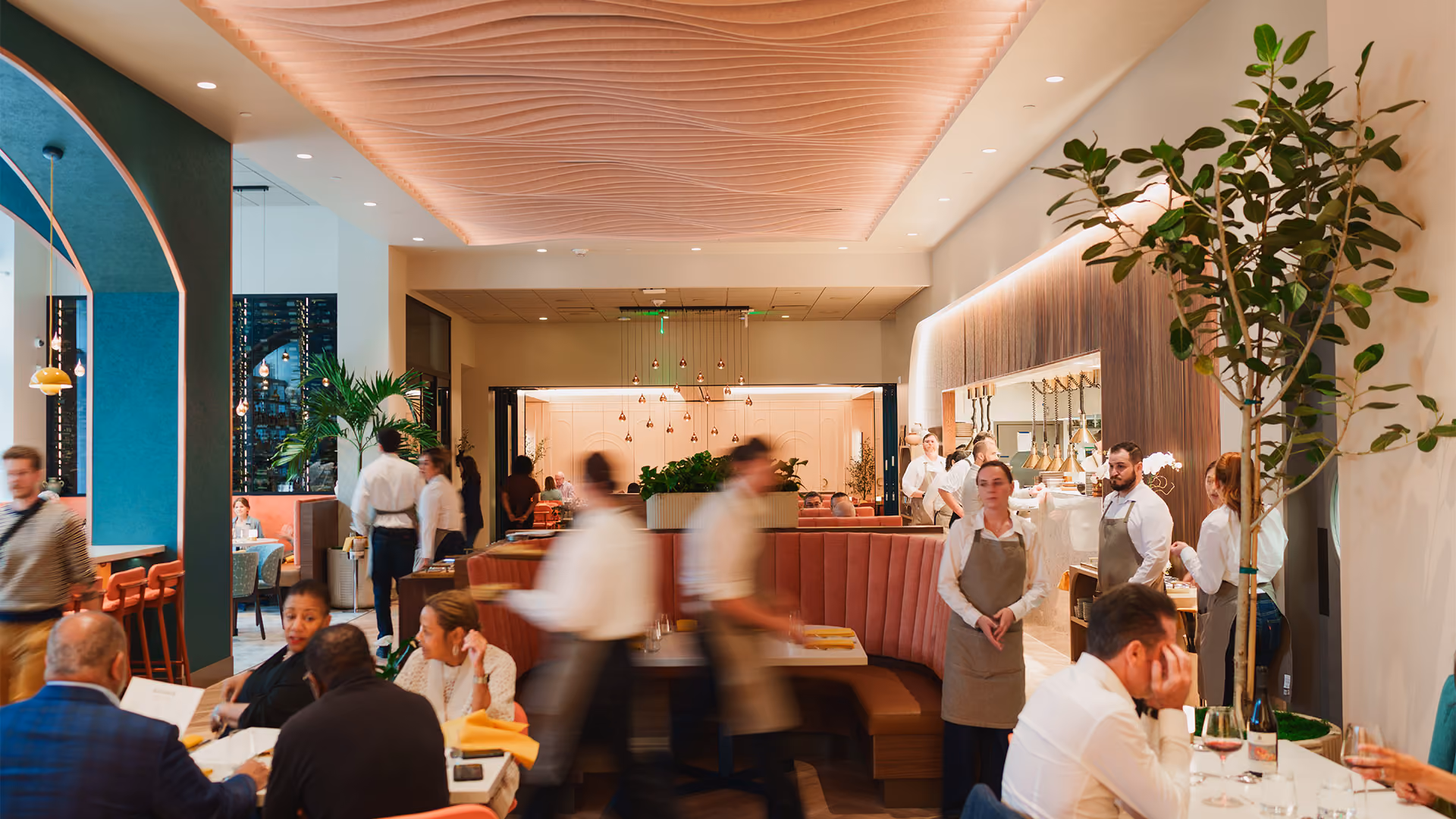 Modern restaurant interior with patrons dining, waitstaff in motion, and warm ambient lighting.