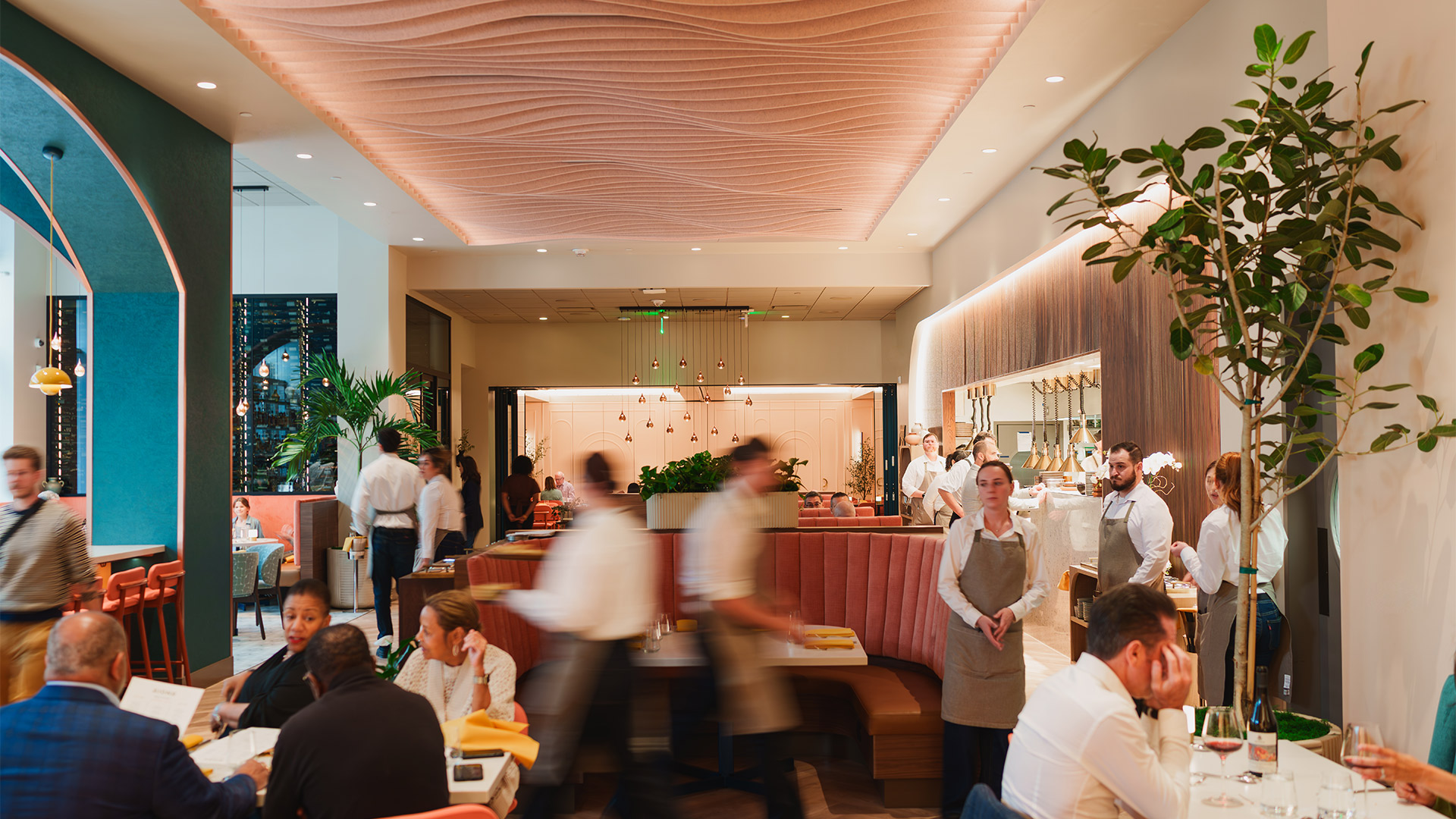 Modern restaurant interior with patrons dining, waitstaff in motion, and warm ambient lighting.