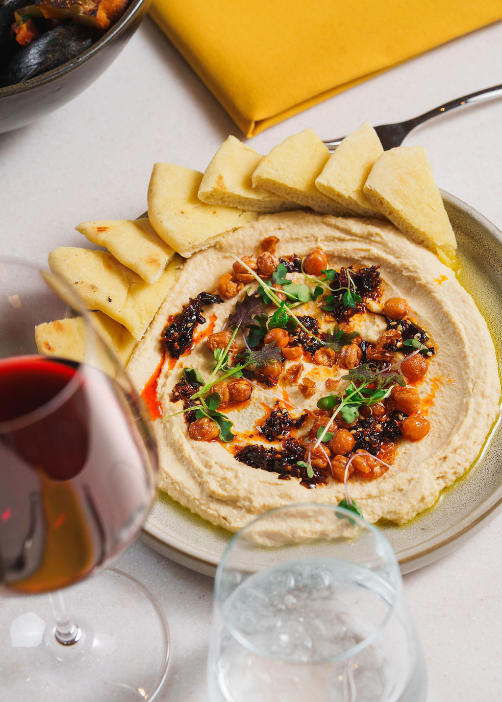 Plate of hummus topped with roasted chickpeas, herbs, and chili oil, served with pita bread triangles.
