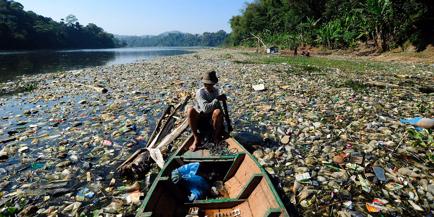 Photo d'une pirogue qui traverse un lac rempli de déchets.