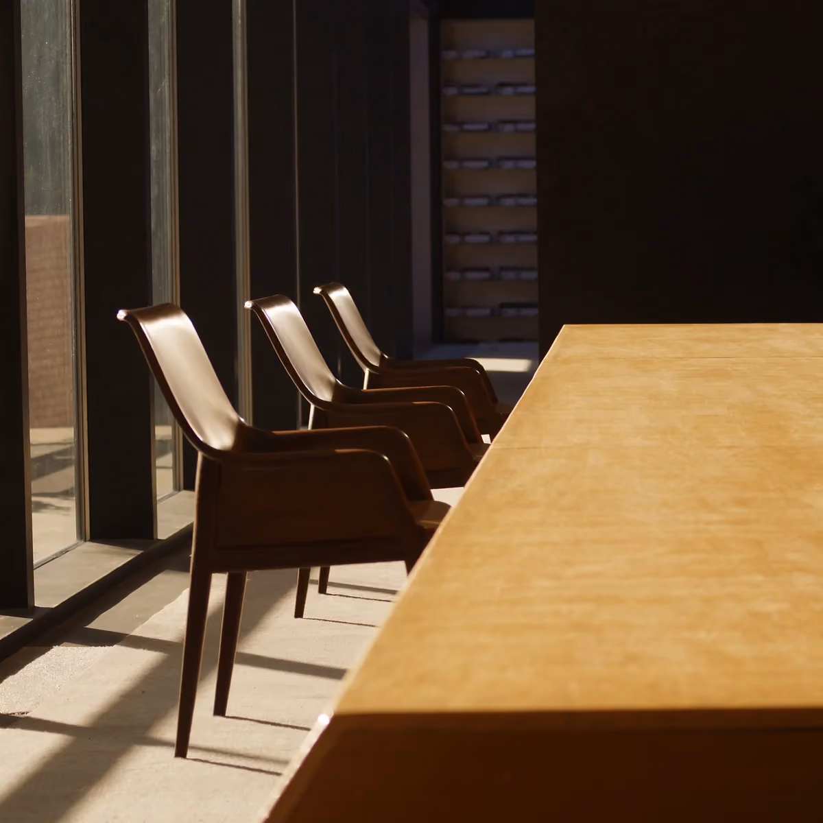 Three chairs in golden-hour light at a long meeting table