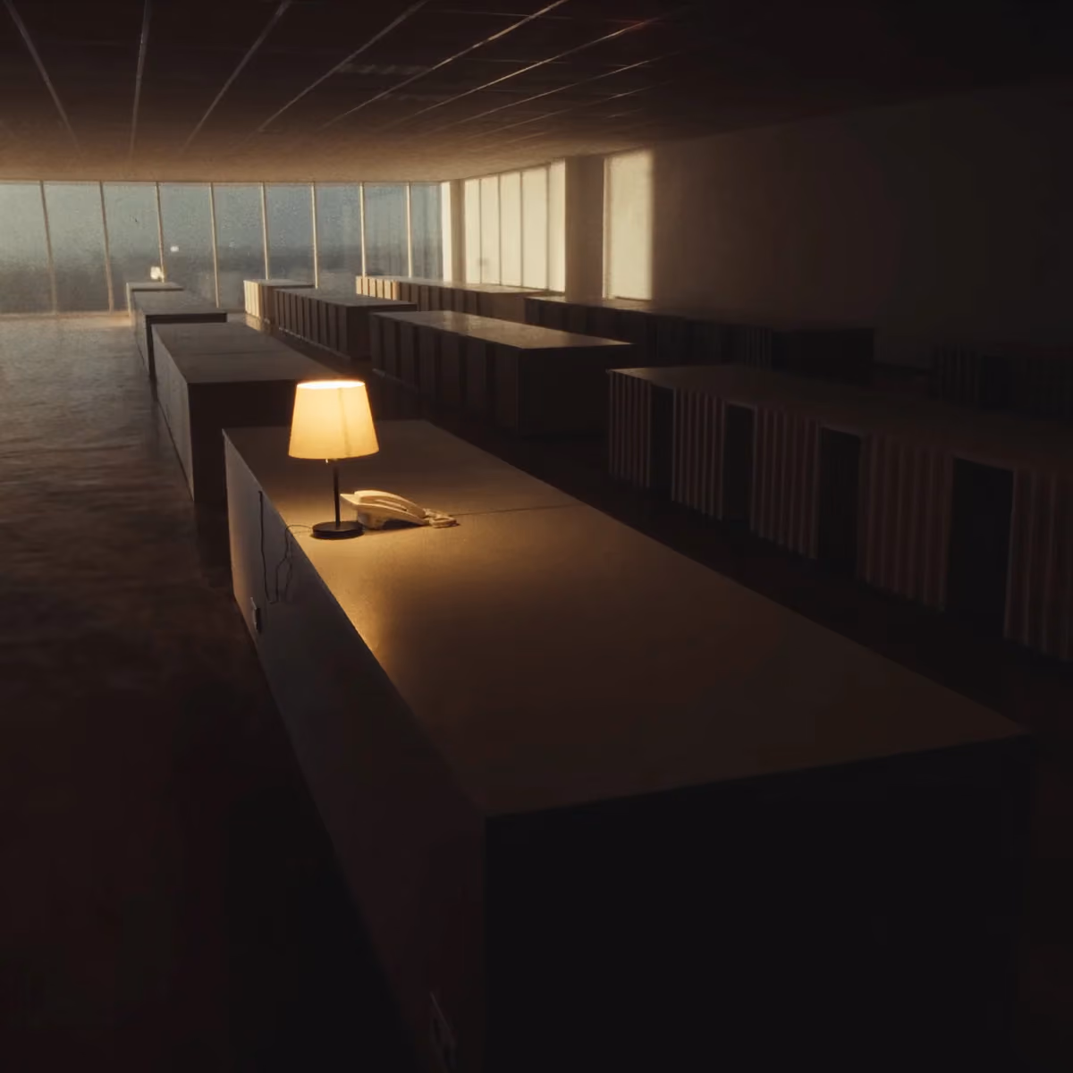A row of desks at dawn with a single lamp and phone glowing