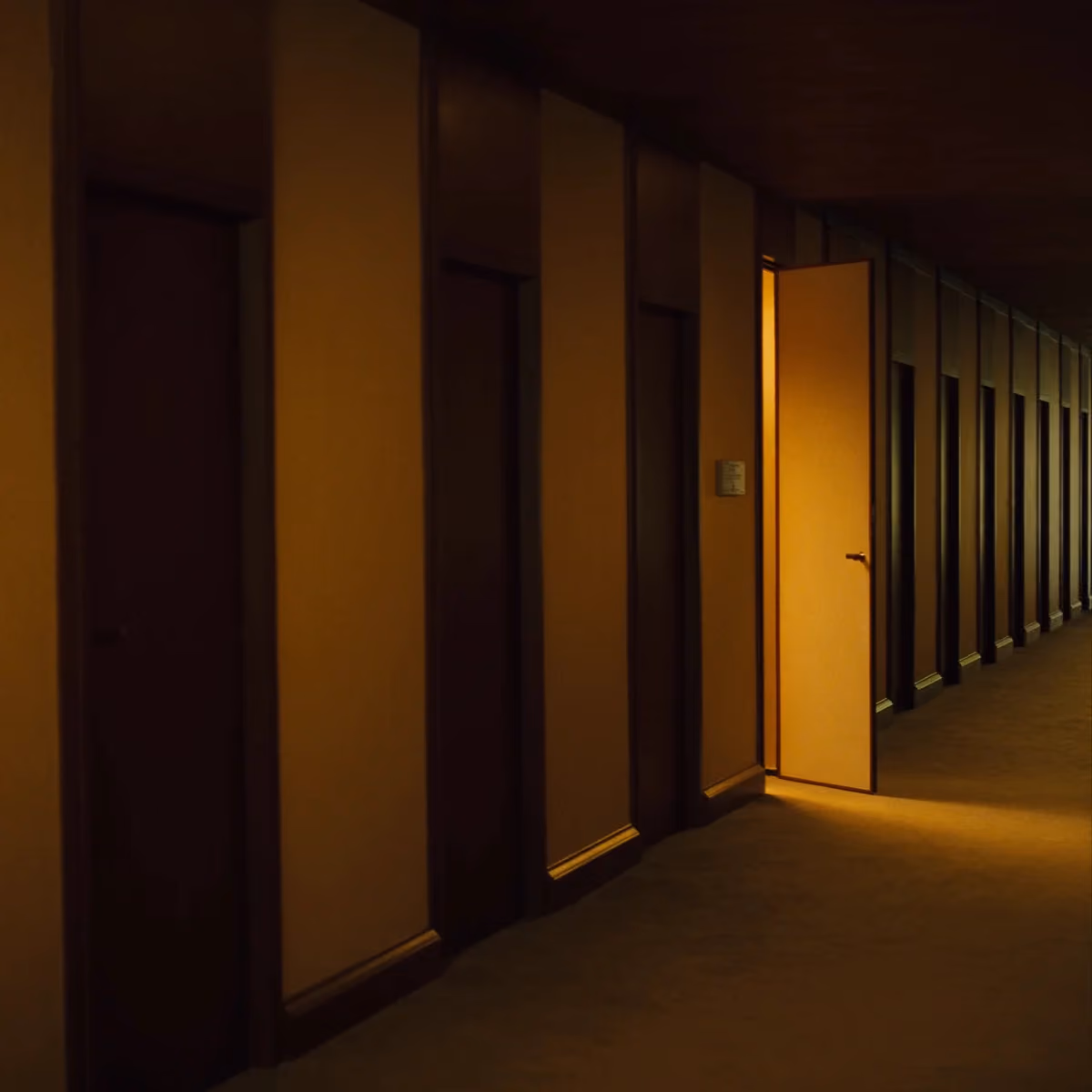 A corridor of office doors with one open, warm light spilling out