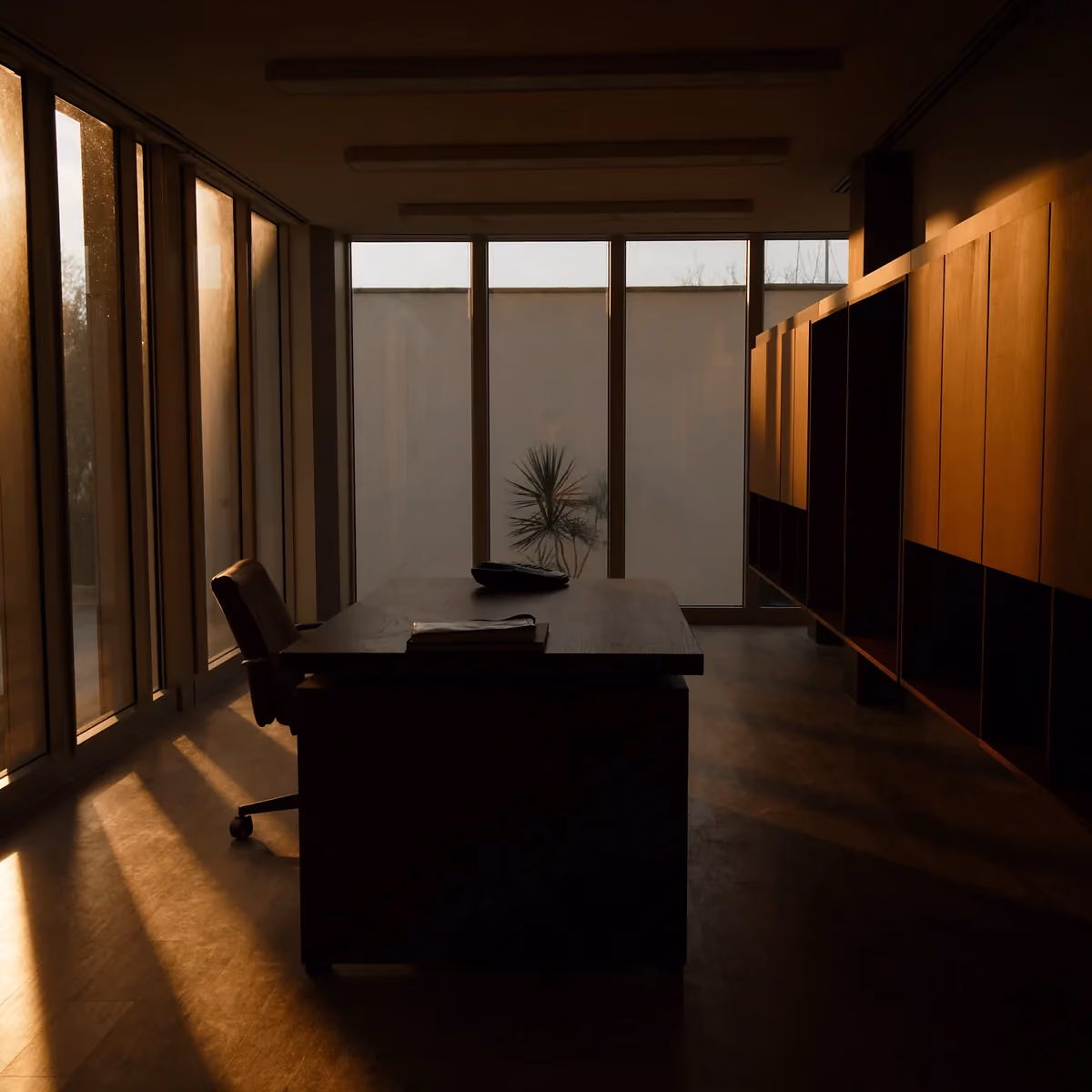 Empty executive office at golden hour, a phone face-down on the desk