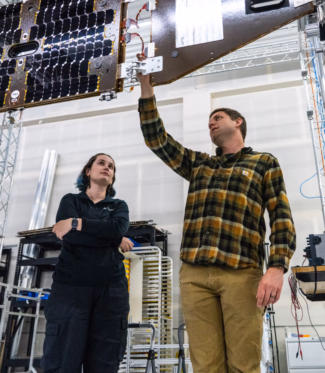 Two engineers inspect a large solar panel inside an industrial facility.