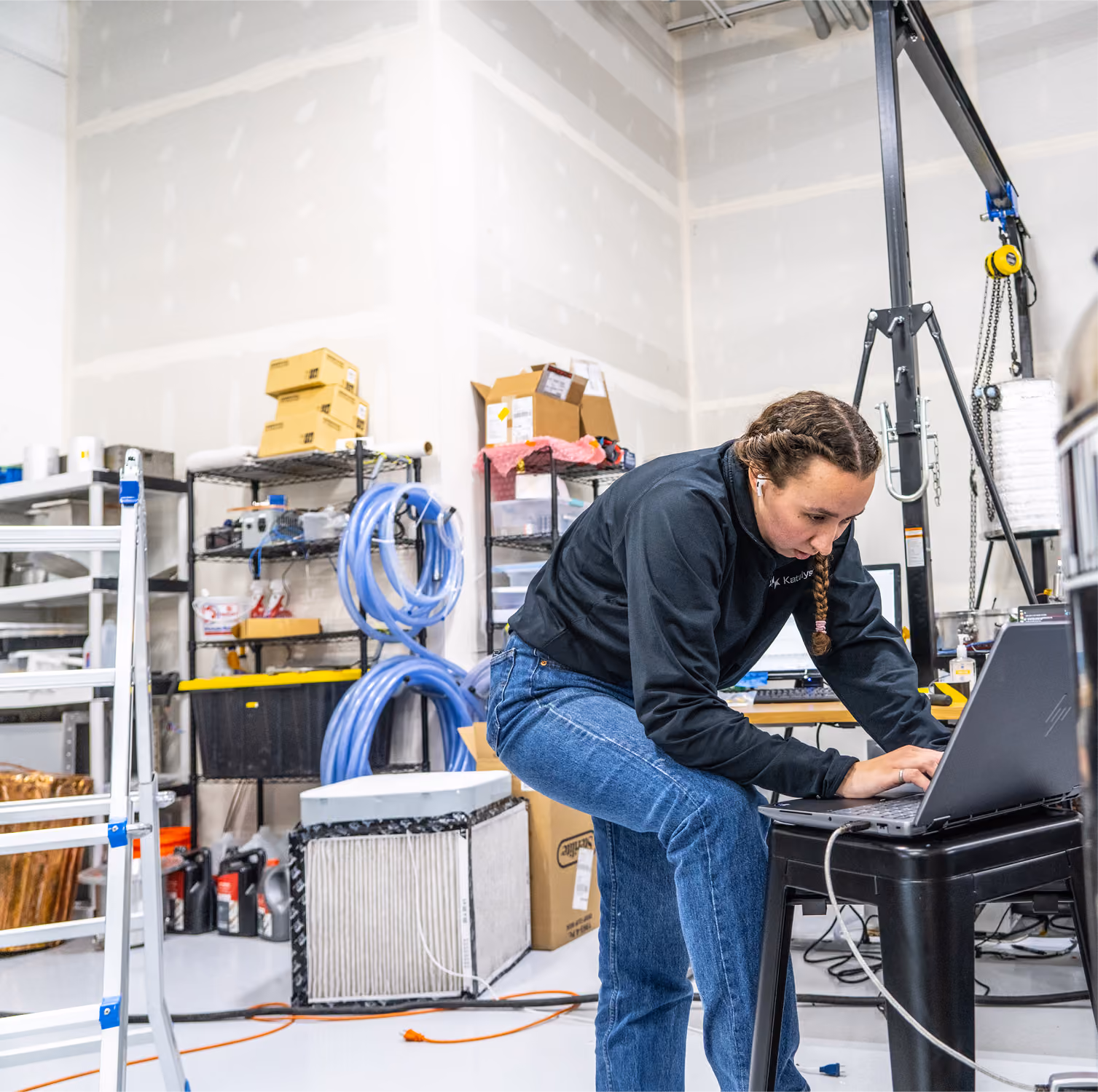 Man with blond hair working on an electronic device on a blue metal surface in a workshop.