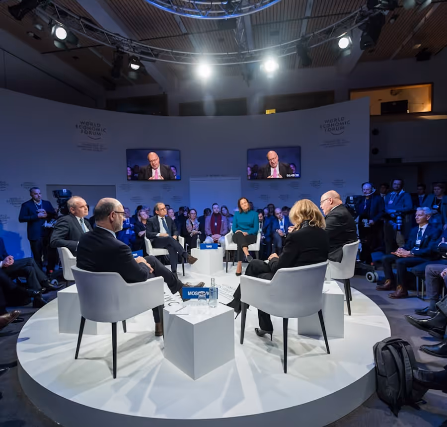Panel discussion at the World Economic Forum with six seated participants on a round stage surrounded by an audience.
