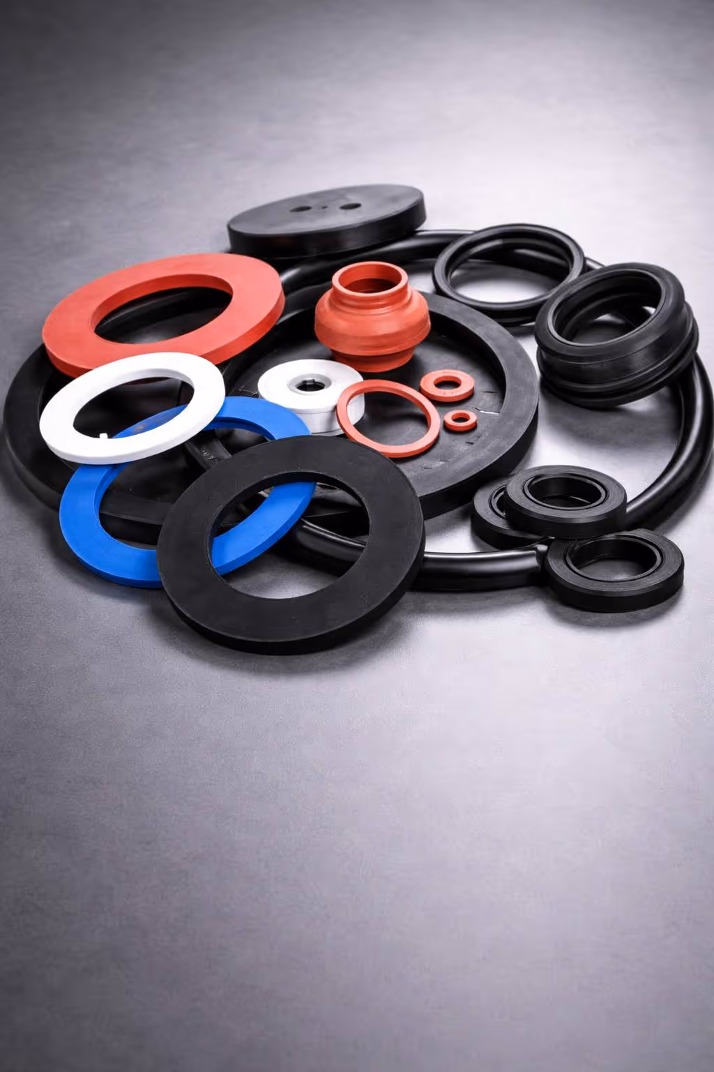 Various rubber gaskets, seals, and O-rings in different colors and sizes arranged on a gray surface.