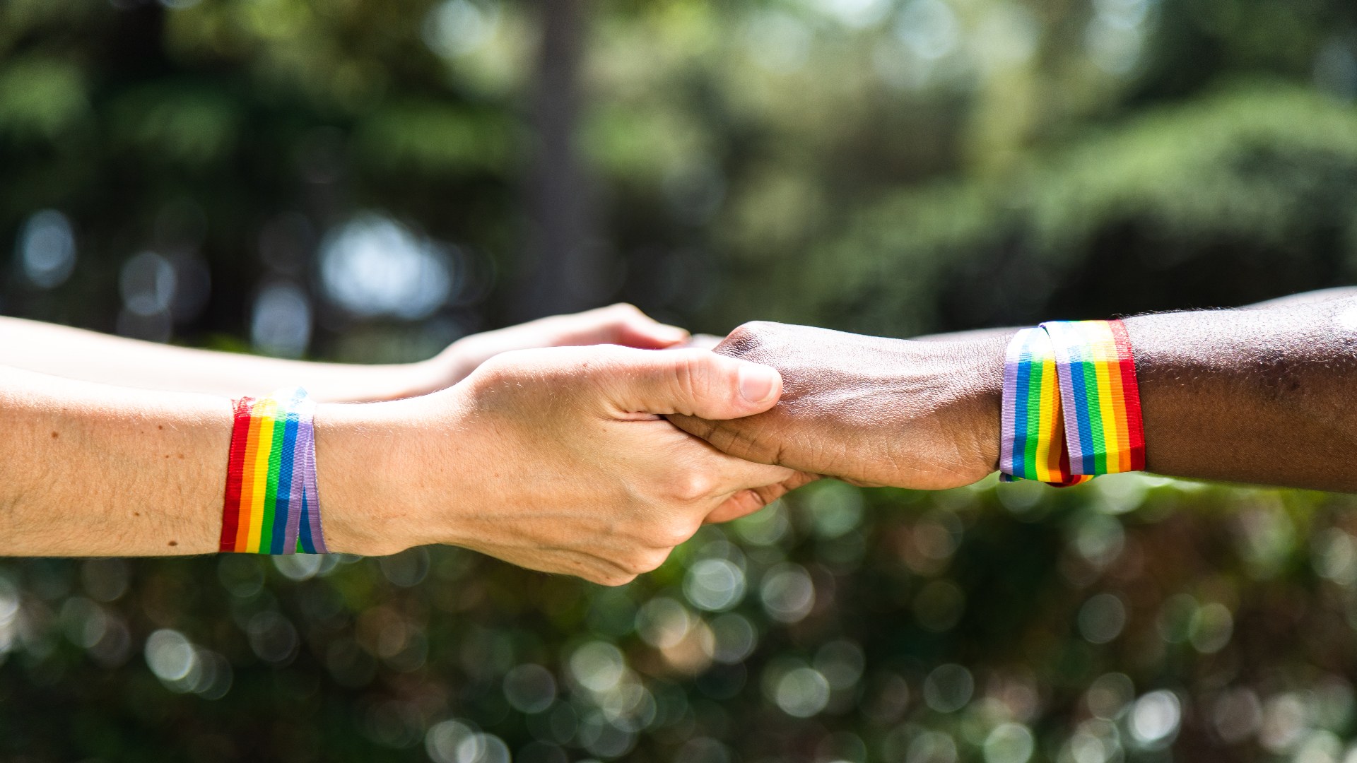 Two people holding hands wearing rainbow Pride wristbands