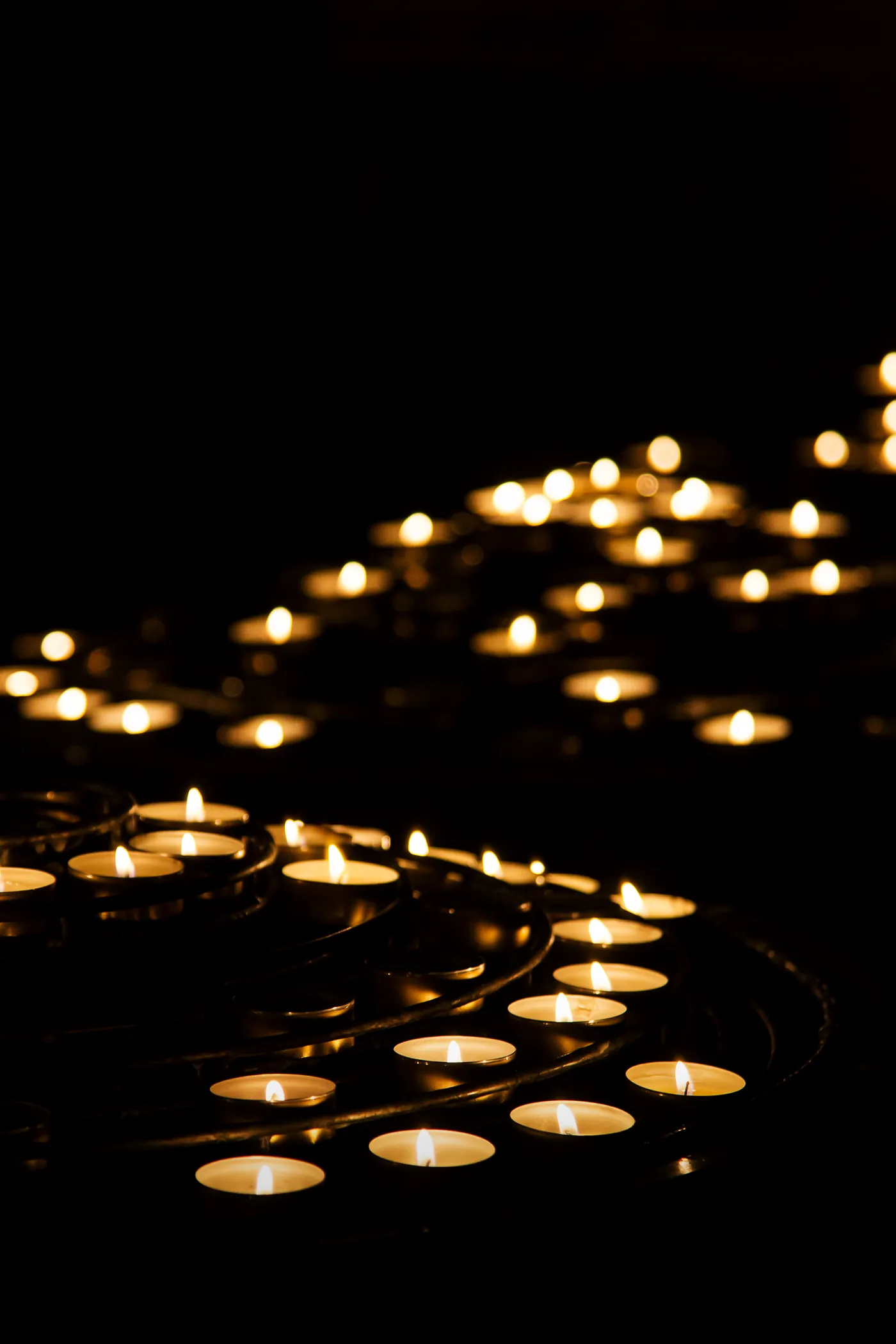 Rows of small lit candles glowing on an iron stand in a dark church